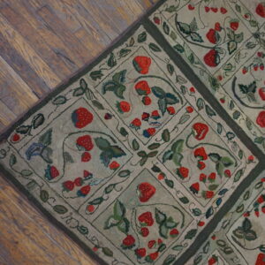 A low-pile rug featuring repeating diamond squares filled with red strawberries and green leaves on wood flooring.
