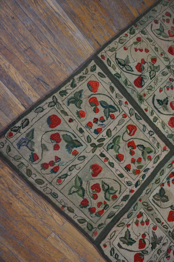 A low-pile rug featuring repeating diamond squares filled with red strawberries and green leaves on wood flooring.