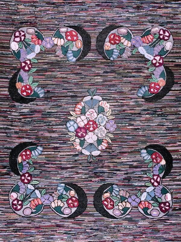A variegated dark looped rug displays symmetrical bright floral motifs around a central bouquet.