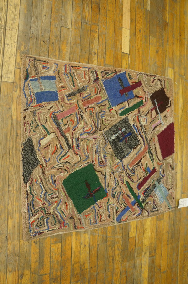 Abstract hooked rug in tan, blue, green, and dark colors rests upon rustic golden wood plank flooring.