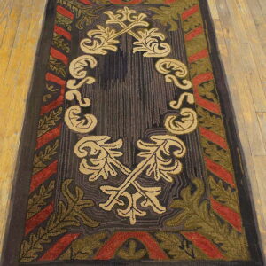 Dark rectangular rug with tan central foliage and a red and olive green patterned border on wood flooring.