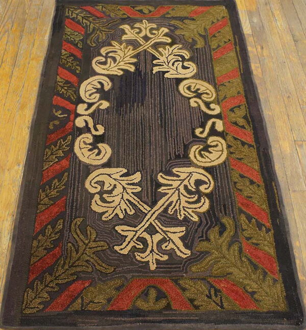 Dark rectangular rug with tan central foliage and a red and olive green patterned border on wood flooring.