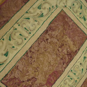 High-pile rug with a maroon central field and a cream border featuring green scrolling patterns on wood floor.