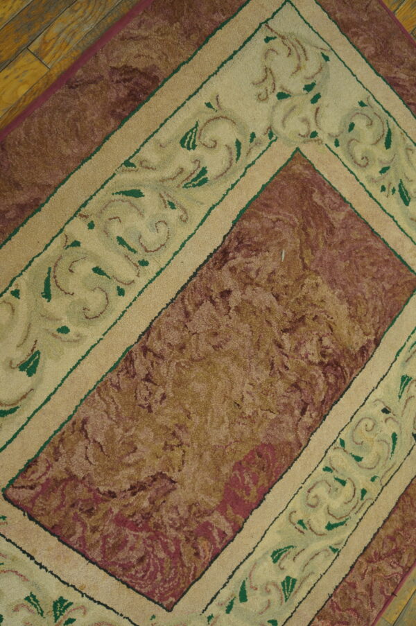 High-pile rug with a maroon central field and a cream border featuring green scrolling patterns on wood floor.