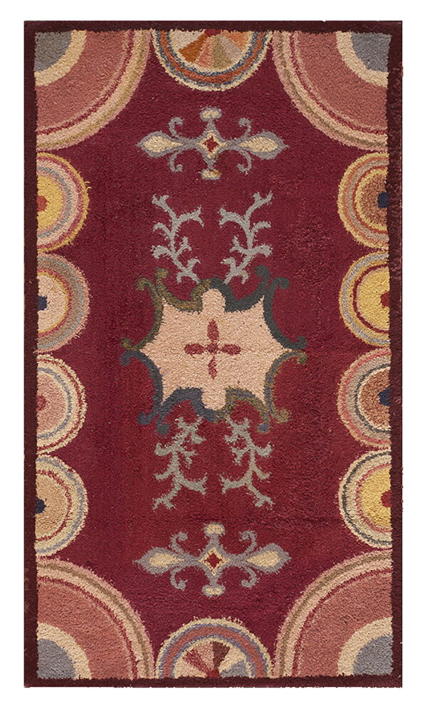 A textured maroon rug features a multicolor geometric and floral central medallion with semicircles around the border.
