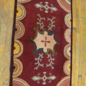 High-pile red rug featuring stylized beige cartouche and colorful circular motifs rests on plank wood flooring.