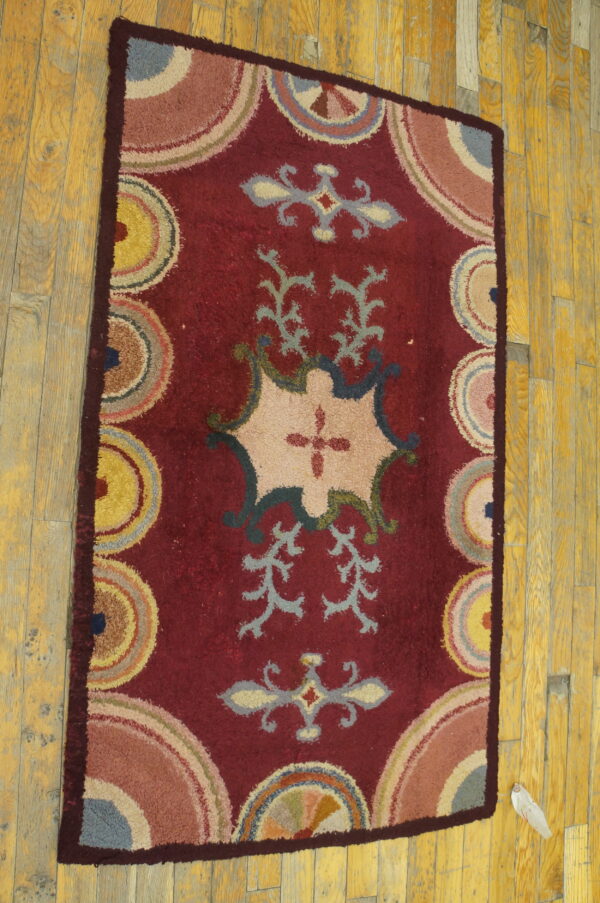 High-pile red rug featuring stylized beige cartouche and colorful circular motifs rests on plank wood flooring.