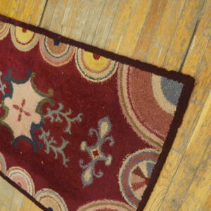 Textured maroon runner rug displaying colorful concentric arcs and floral designs on distressed wood flooring.