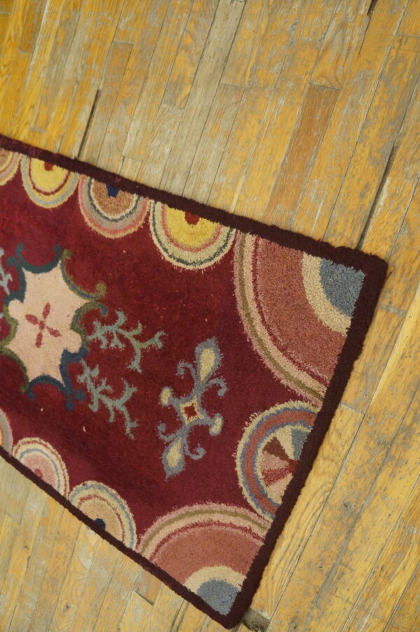 Textured maroon runner rug displaying colorful concentric arcs and floral designs on distressed wood flooring.