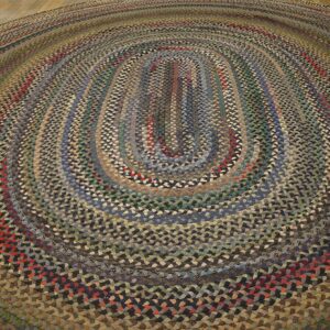 Oval braided rug in varied shades of brown, gray, green, and red on light wood floor.