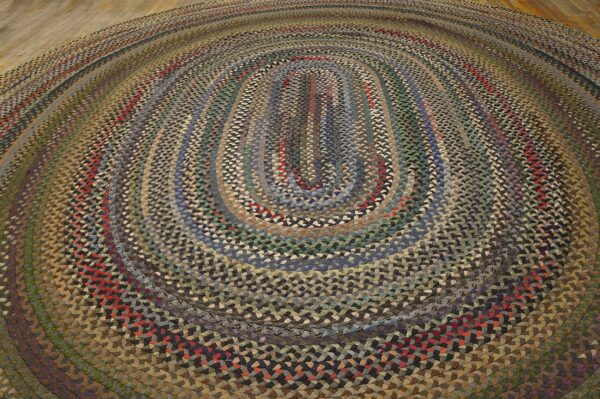 Oval braided rug in varied shades of brown, gray, green, and red on light wood floor.