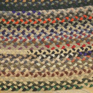 Chunky, multicolored braided rug composed of concentric rows of various patterned and solid fabric strips on wood floor.