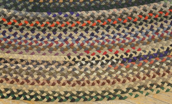 Chunky, multicolored braided rug composed of concentric rows of various patterned and solid fabric strips on wood floor.