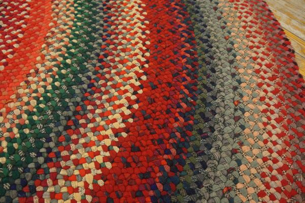 Close view of a multicolored braided rug with red, green, and gray stripes on distressed wood flooring.