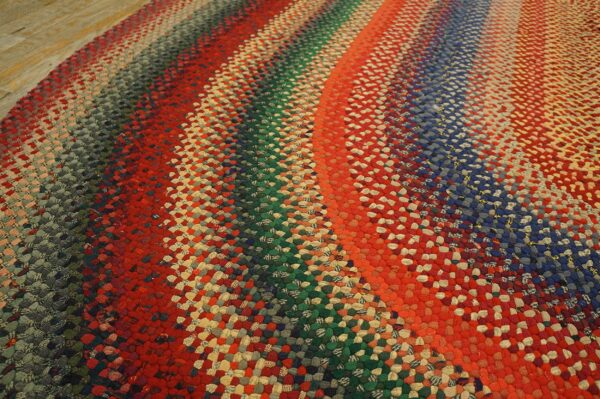Textured braided rug in vibrant concentric stripes of red, blue, green, and mixed colors on wood flooring.