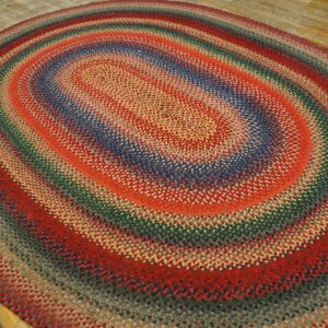 Multicolored braided oval rug featuring concentric bands of red, blue, green, and gray on a wood floor.