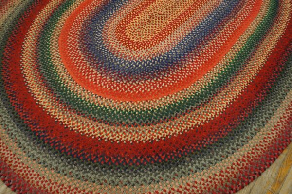 Highly textured braided rug with colorful concentric oval rings in red, blue, green, and gray tones.