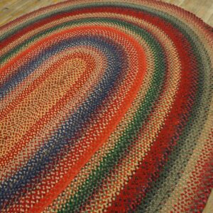 A textured, braided, multicolored oval rug with banded rings lies on light, worn wooden flooring.