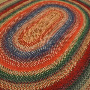 An oval braided rug with thick concentric stripes of red, blue, green, and gray upon wood flooring.