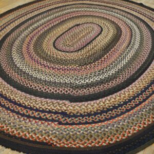 Multicolored braided oval rug with concentric rings in brown, blue, pink, and gray on a wooden floor.