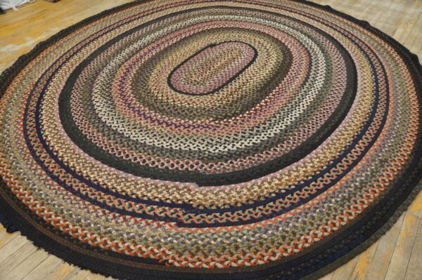 Multicolored braided oval rug with concentric rings in brown, blue, pink, and gray on a wooden floor.