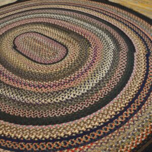 Oval braided rug in multicolor tones of pink, brown, and navy resting on light wood floorboards.