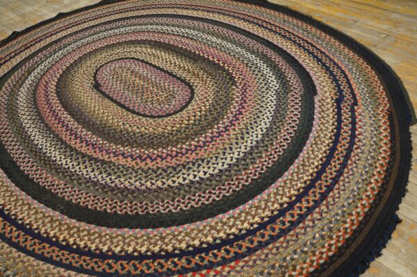 Oval braided rug in multicolor tones of pink, brown, and navy resting on light wood floorboards.