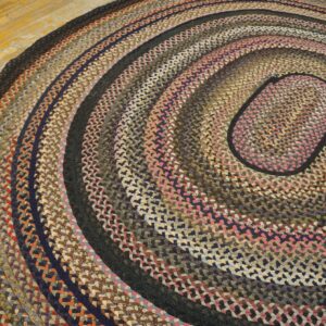Braided rug with concentric rings of brown, navy, black, and pink textiles on a wood floor.