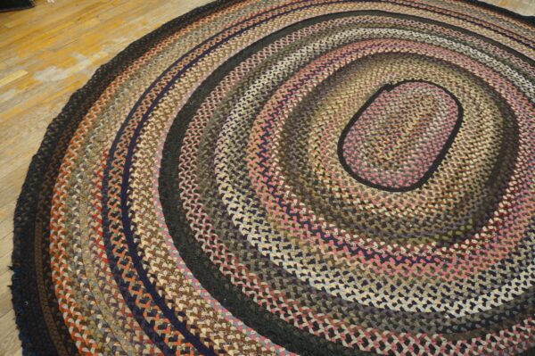 Braided rug with concentric rings of brown, navy, black, and pink textiles on a wood floor.
