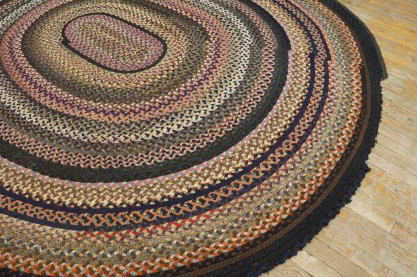 Multicolored braided oval rug with pink, tan, navy, and brown concentric rings on distressed wood flooring.