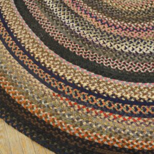 Multicolored braided round rug with concentric dark, rust, pink, and brown rings on a wood floor.