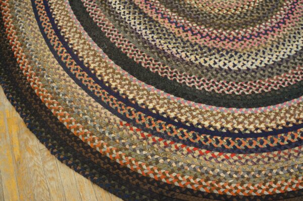 Multicolored braided round rug with concentric dark, rust, pink, and brown rings on a wood floor.