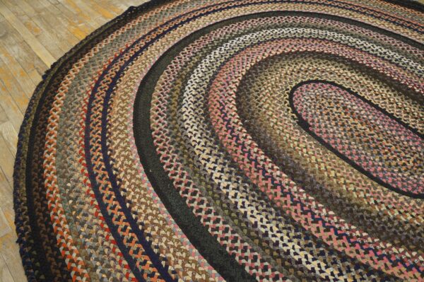 Round, braided rug displaying variegated rings of pink, brown, navy, and rust resting on aged wooden floorboards.