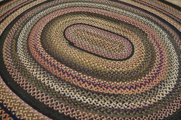 Low-pile braided oval rug with concentric rings in brown, pink, gray, and multicolored blends.