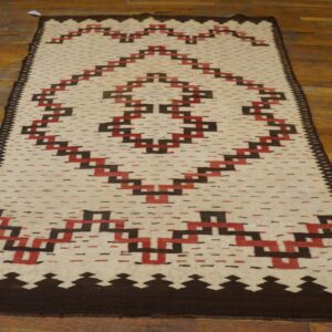 Cream runner rug with stepped dark brown and red geometric design lying on worn wooden floors.