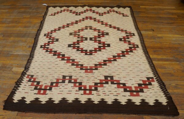 Cream runner rug with stepped dark brown and red geometric design lying on worn wooden floors.