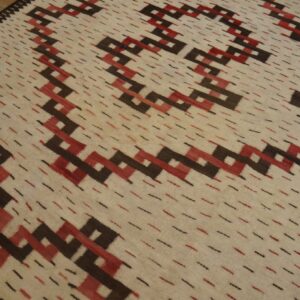 A cream rug with diagonal dark brown and red geometric patterns rests on rustic wood planks.