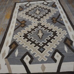 A flatwoven rug featuring large stepped diamond patterns in gray, brown, and cream rests on distressed wood.