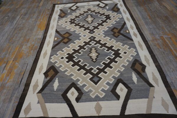 A flatwoven rug featuring large stepped diamond patterns in gray, brown, and cream rests on distressed wood.