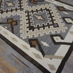 Flatweave rug displaying a geometric pattern in gray, brown, cream, and tan on distressed gray wood floors.
