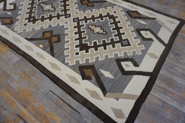 Flatweave rug displaying a geometric pattern in gray, brown, cream, and tan on distressed gray wood floors.