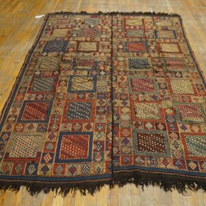 Complex geometric rug in red, blue, and gold tones lying on distressed hardwood planks.