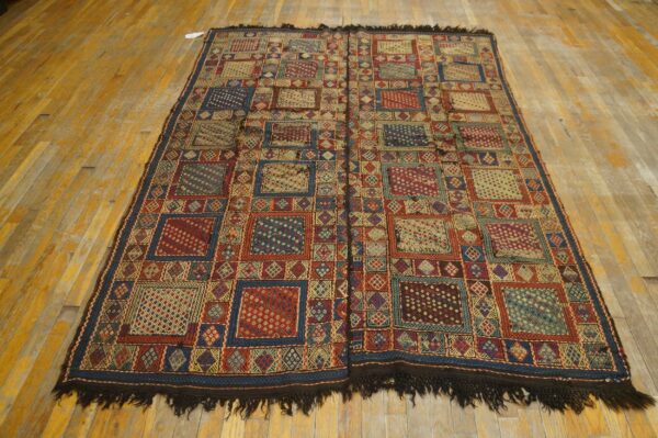 Complex geometric rug in red, blue, and gold tones lying on distressed hardwood planks.