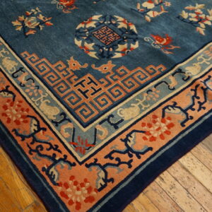 Corner view of a blue patterned rug showing salmon and teal geometric borders on plank wood flooring.