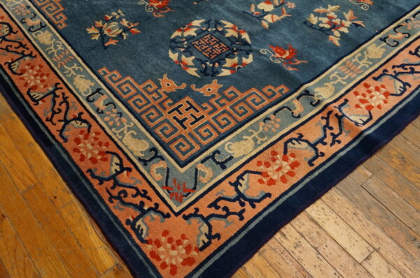 Corner view of a blue patterned rug showing salmon and teal geometric borders on plank wood flooring.