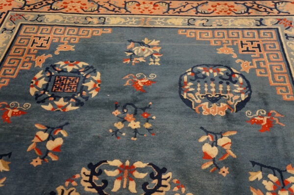 Close-up of a dusty blue rug showing peach and navy oriental motifs, including a greek key border.