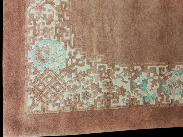 Plush mauve rug corner with an embossed border of ivory, dusty rose, and light teal floral designs.