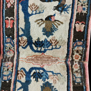 High-pile rug with a cream field, blue trees, brown bird, and dark border featuring pink butterflies.