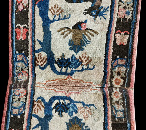 High-pile rug with a cream field, blue trees, brown bird, and dark border featuring pink butterflies.