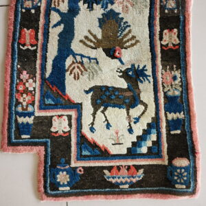 High-pile, dark-bordered rug featuring blue and brown animal figures on a cream ground with pink and rust accents.